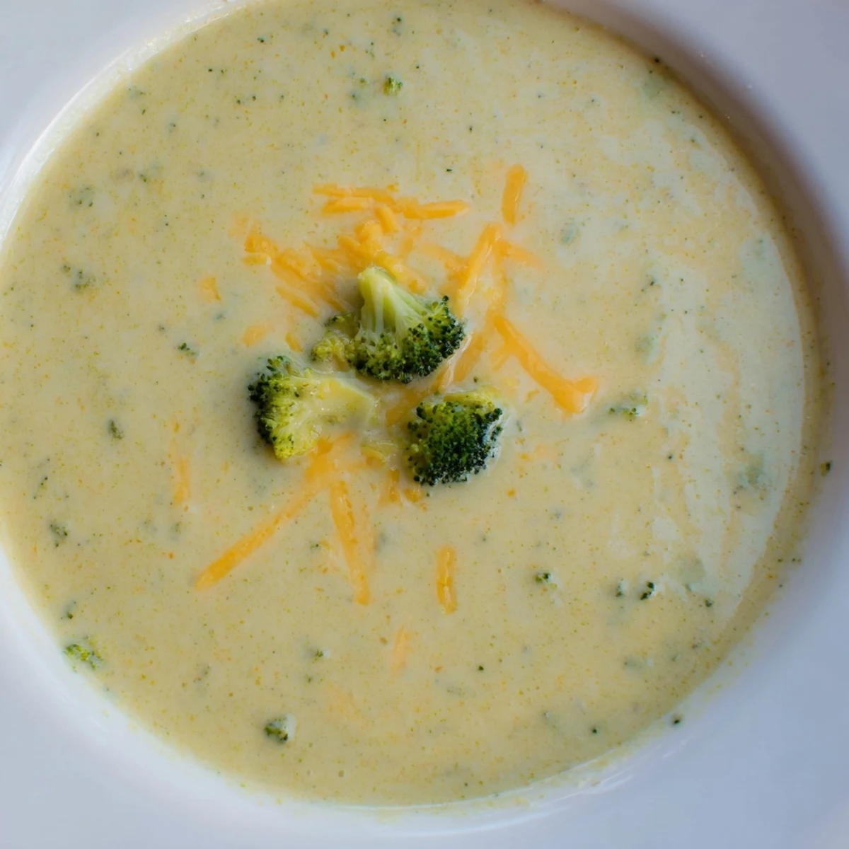 Golden roasted broccoli florets swimming in rich, creamy cheddar soup, steaming warmly in a ceramic bowl ready to enjoy.