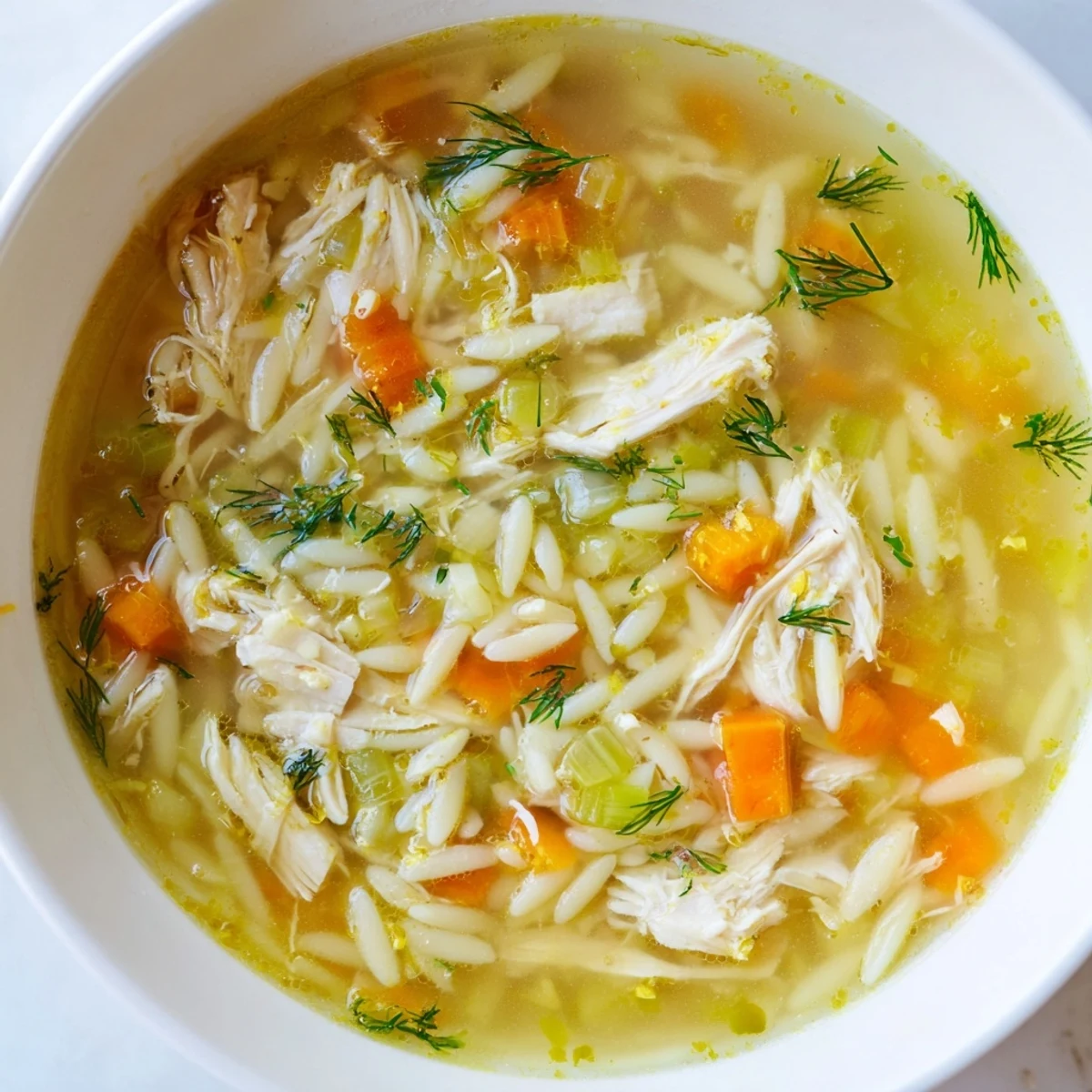 A comforting bowl of Chicken Lemon Orzo Soup with tender chicken, bright lemon, and orzo pasta, garnished with fresh dill.