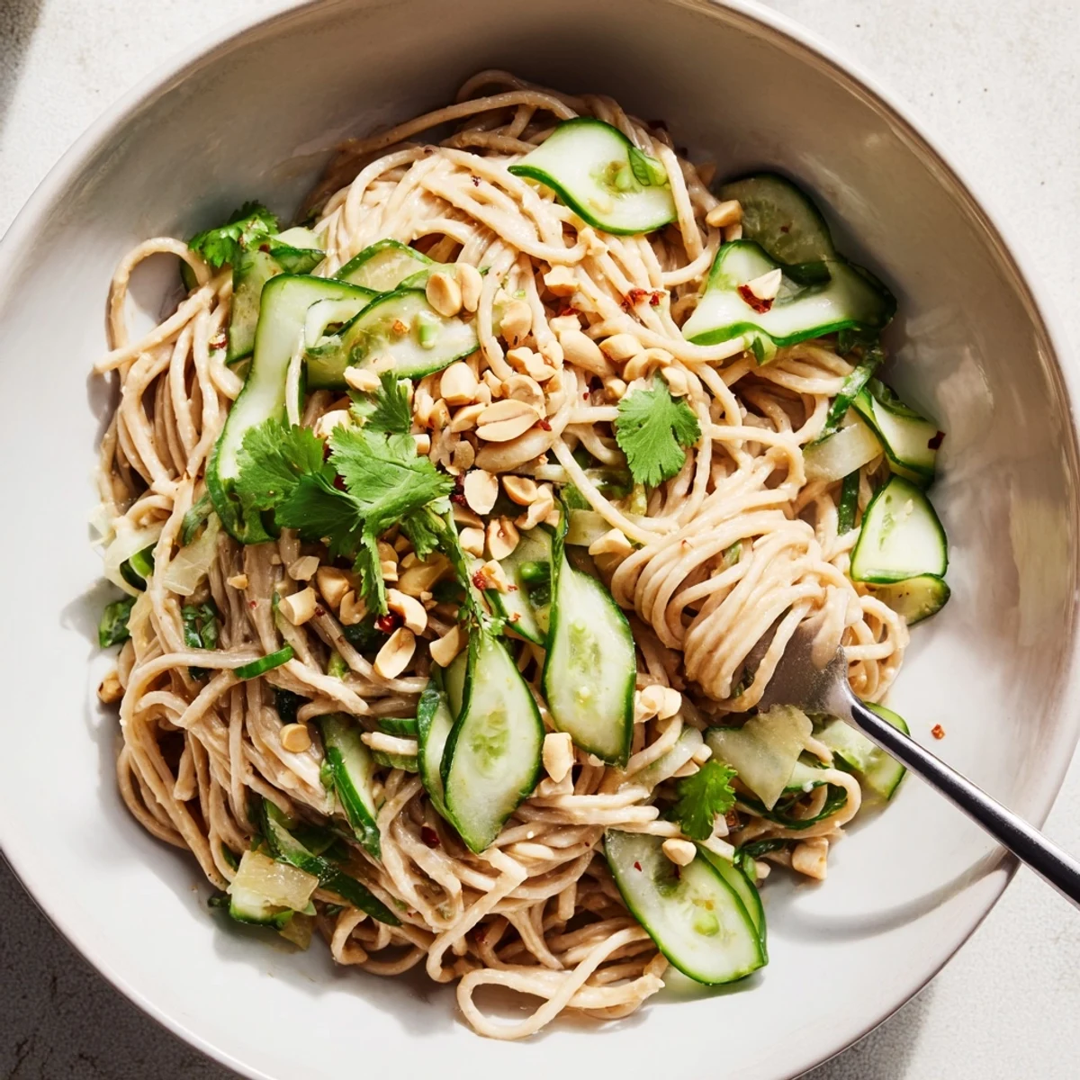 Vibrant bowl of Spicy Sesame Noodle Salad featuring julienned cucumbers, sesame seeds, and herbs.  