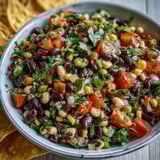 Freshly tossed Cowboy Caviar dip surrounded by crunchy tortilla chips, ready for a zesty party appetizer.