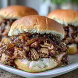 Slow-cooked Applesauce Pulled Pork Sandwiches served warm with a side of tangy coleslaw and crisp pickle chips.