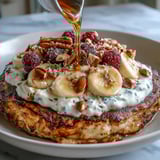 A fluffy Protein Pancake Bowl stacked with sliced bananas, crunchy nuts, and a generous drizzle of nut butter for a hearty breakfast.