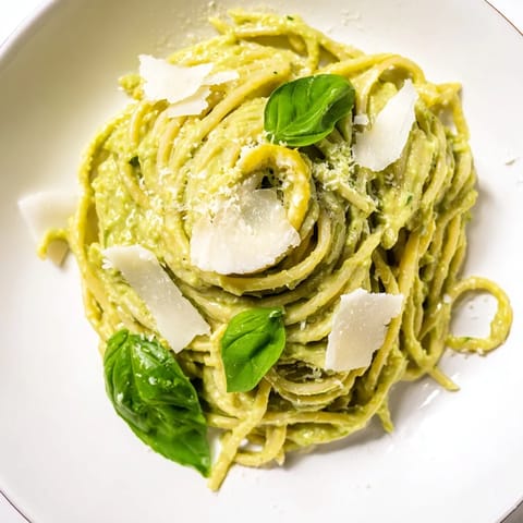 Tossed creamy avocado pasta, garnished with fresh basil and Parmesan, ready for a satisfying dinner.