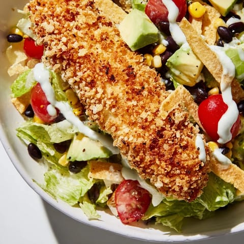 Tortilla strips and creamy salsa ranch dressing drizzled over a hearty Crispy Chicken Taco Salad bowl.