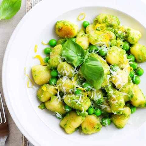 A steaming bowl of Pesto Pea Gnocchi Skillet garnished with fresh basil and parmesan, served for a family-style meal.  