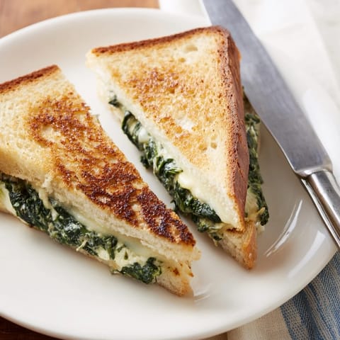 A close-up of golden-brown Feta & Spinach Stuffed Grilled Cheese, oozing melted feta and spinach from thick sourdough slices.  