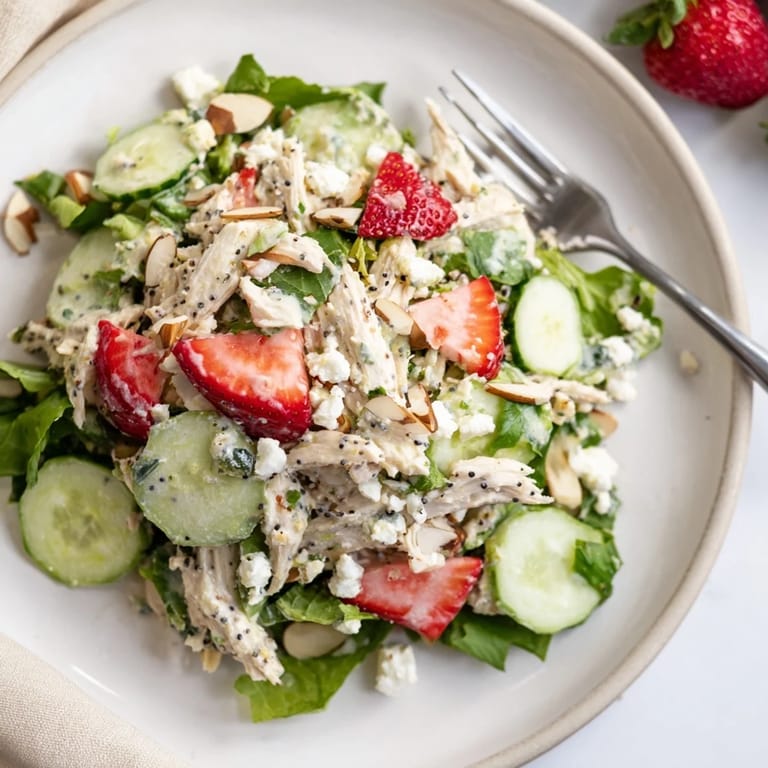 A close-up of shredded chicken salad with juicy strawberries, toasted almonds, and crumbled feta, tossed in creamy poppy seed dressing.  